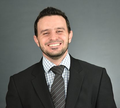 Headshot of Fabio Castro, wearing a black jacket, plaid shirt, and striped tie