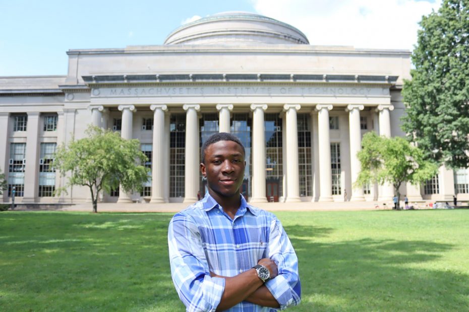 Headshot photo of African American male wearing a blue plaid shirt standing in front of the MIT great dome with his arms crossed
