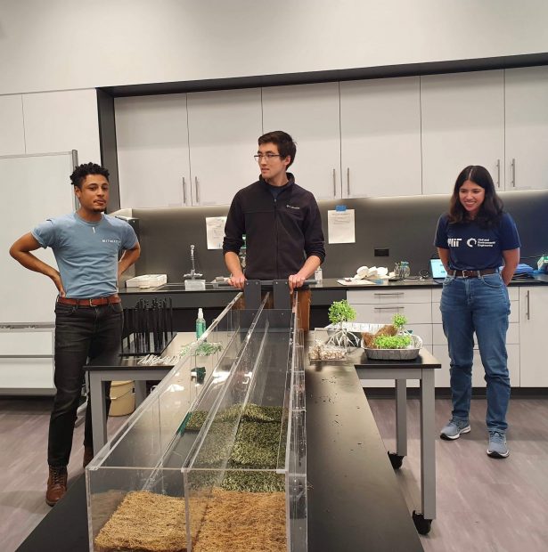 Two male graduate students and one female graduate student standing in front of a flume demonstration