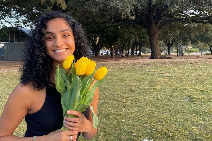 Shailey Patel sitting in a grassy field holding a bouquet of yellow tulips.
