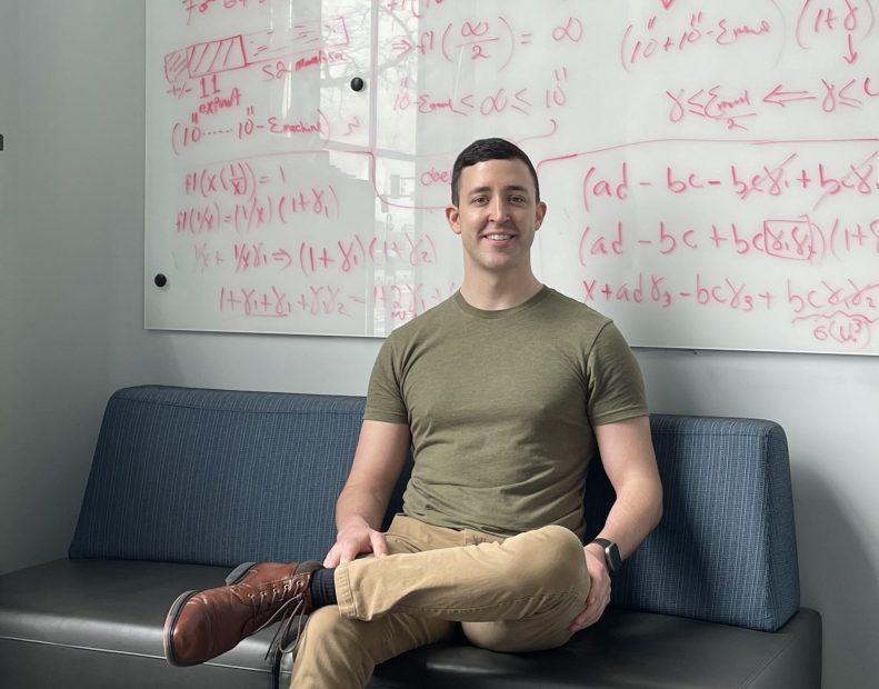 Justin Cole sitting in front of a whiteboard with equations written on it.
